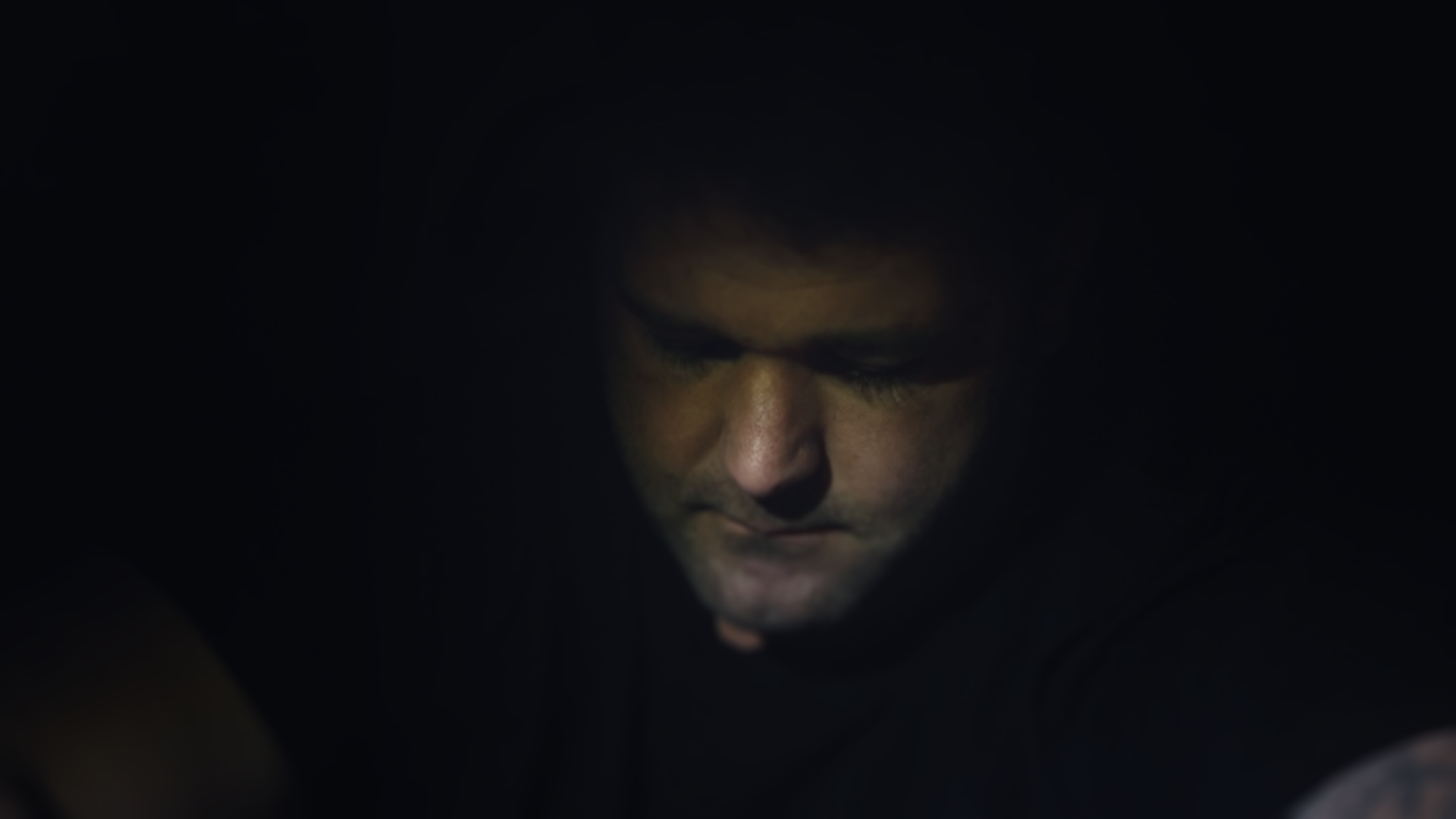 Chiaroscuro portrait of Kenny looking downwards, in very low light