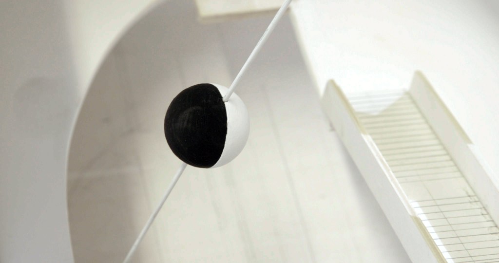 An interesting looking sphere, half black and half white, held up in the air by a thin white horizontal rod