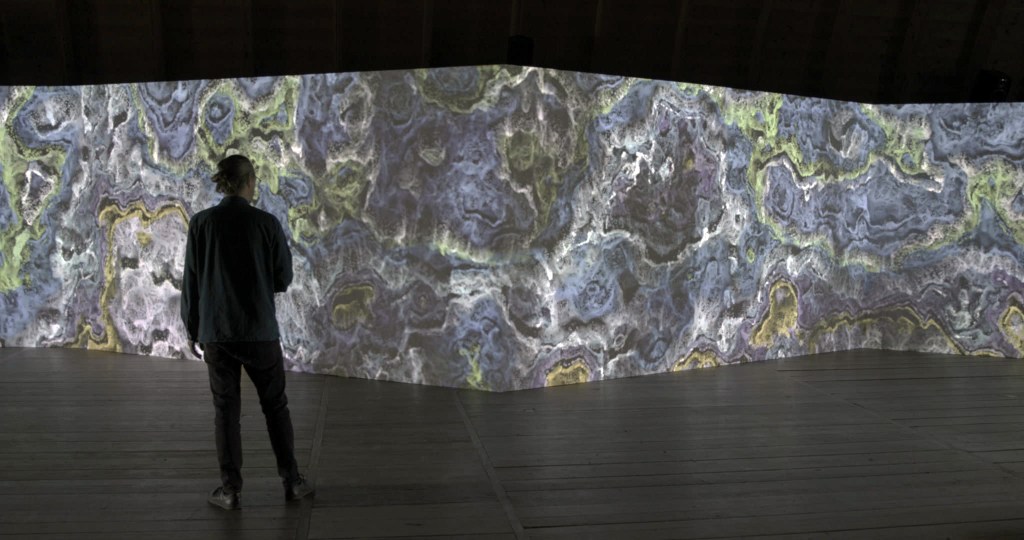 A figure in a gallery space watches a video installation
