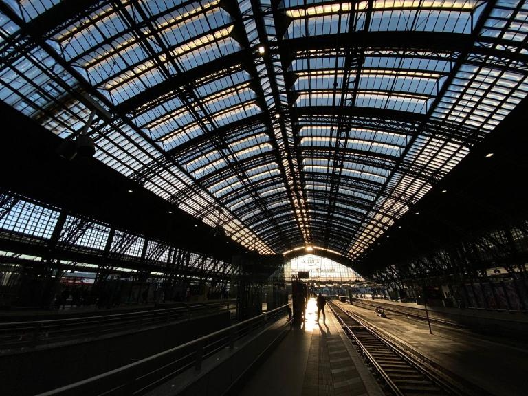 Photo of a railway station platform, a massive glass and steel arched roof above, with golden light streaming in.